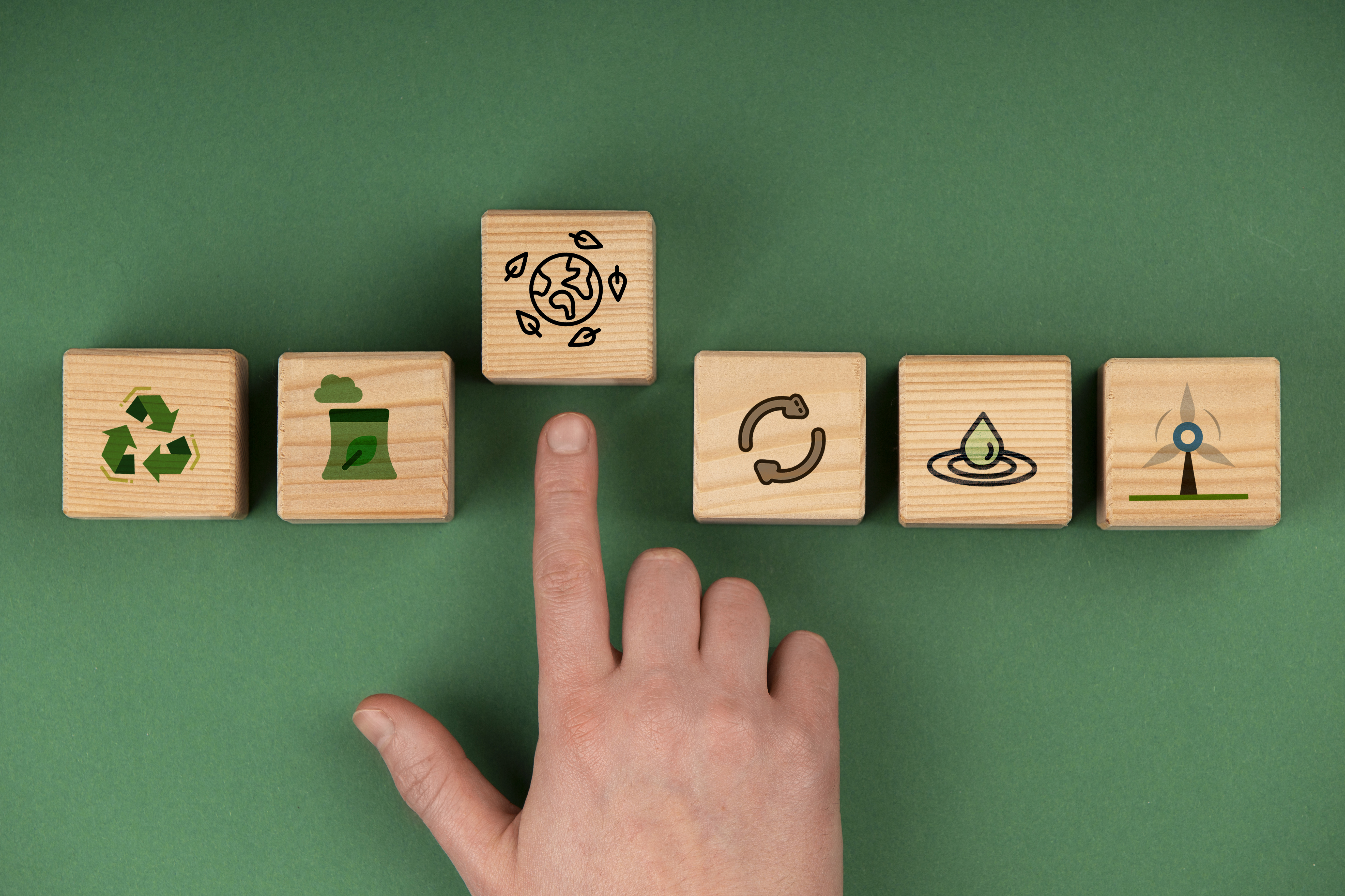 Bloques de madera con iconos de sostenibilidad y una mano se&ntilde;alando el planeta, simbolizando acciones para reducir la huella de carbono